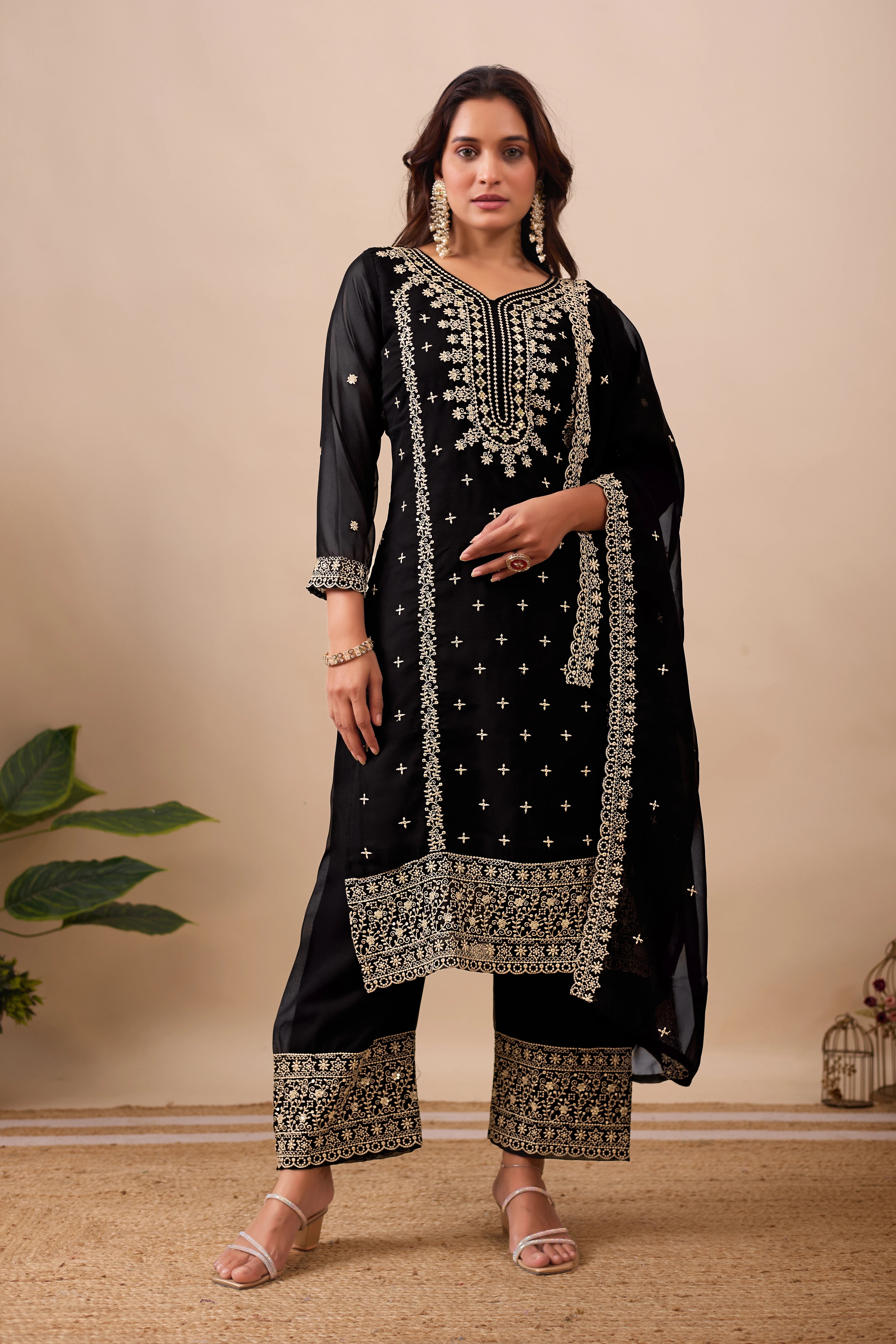 Woman wearing a black embroidered traditional outfit with gold details on a beige background